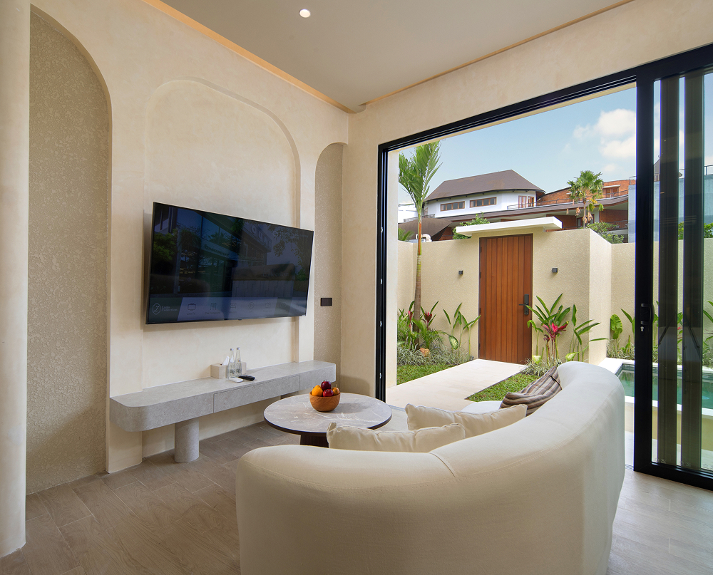 Living room with curved cream sofa and wall-mounted TV, sliding doors open to the pool garden and entrance door