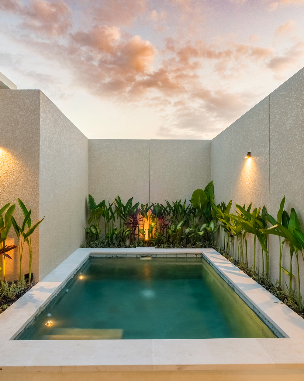 Private plunge pool in a walled tropical garden at dusk, lit by warm wall lights
