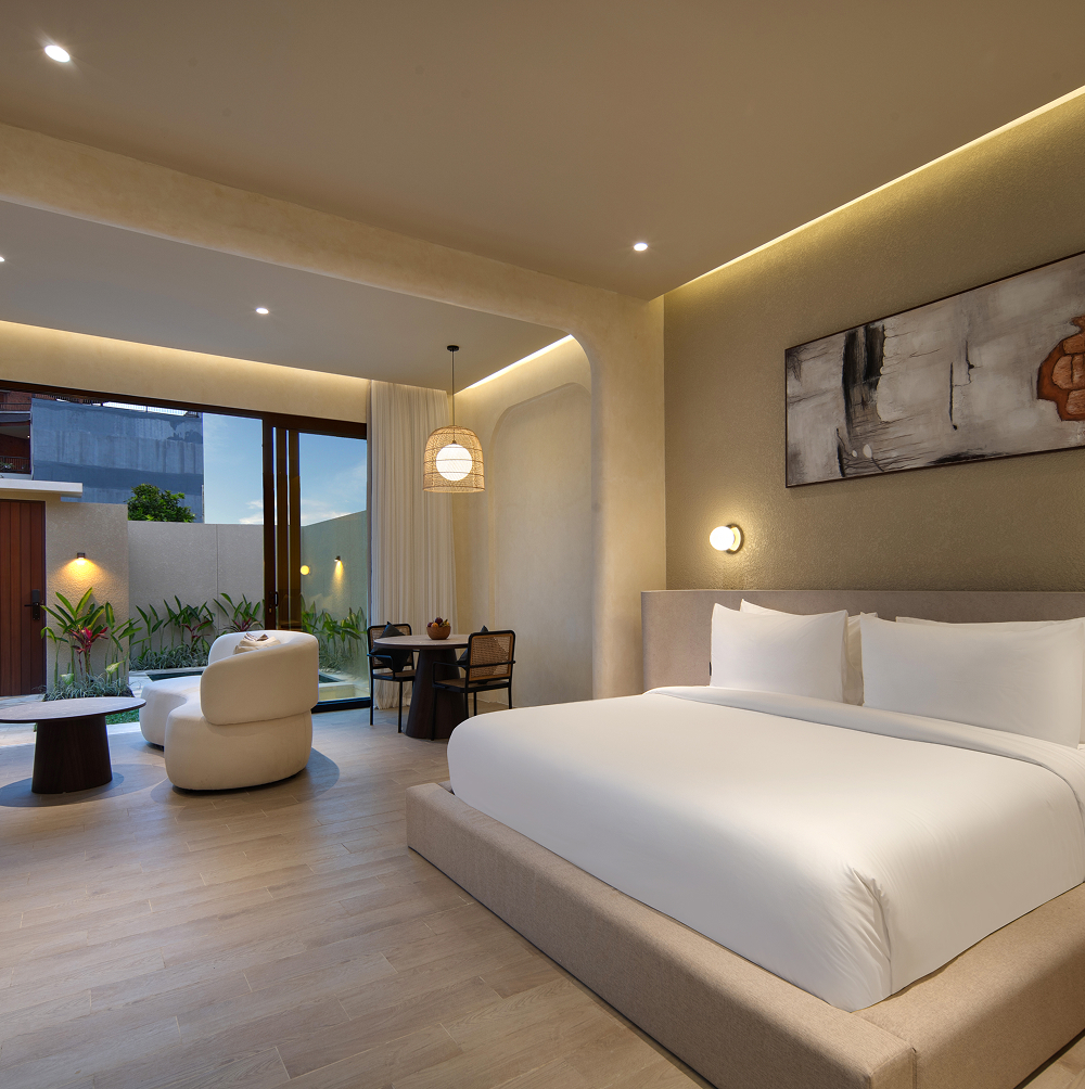 Villa bedroom with king bed, abstract artwork and warm cove lighting, opening onto a lounge and the garden
